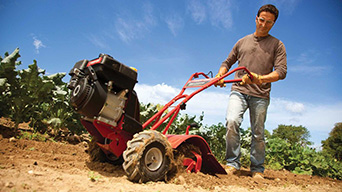 man pushing a red garden tiller